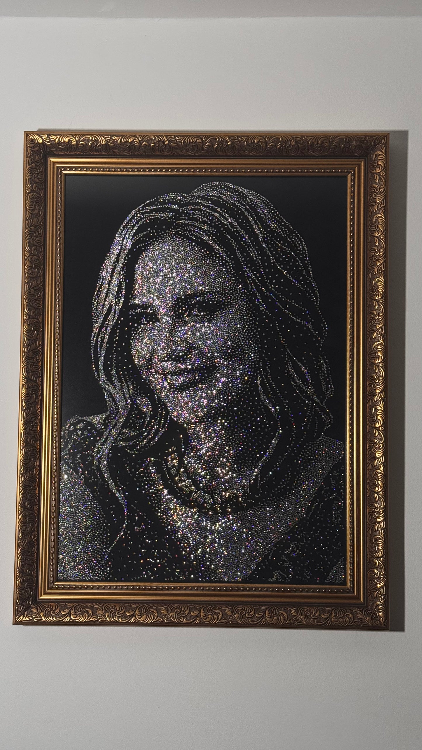Framed artwork of a woman's face made from small, reflective pieces, rhinestones on a dark background