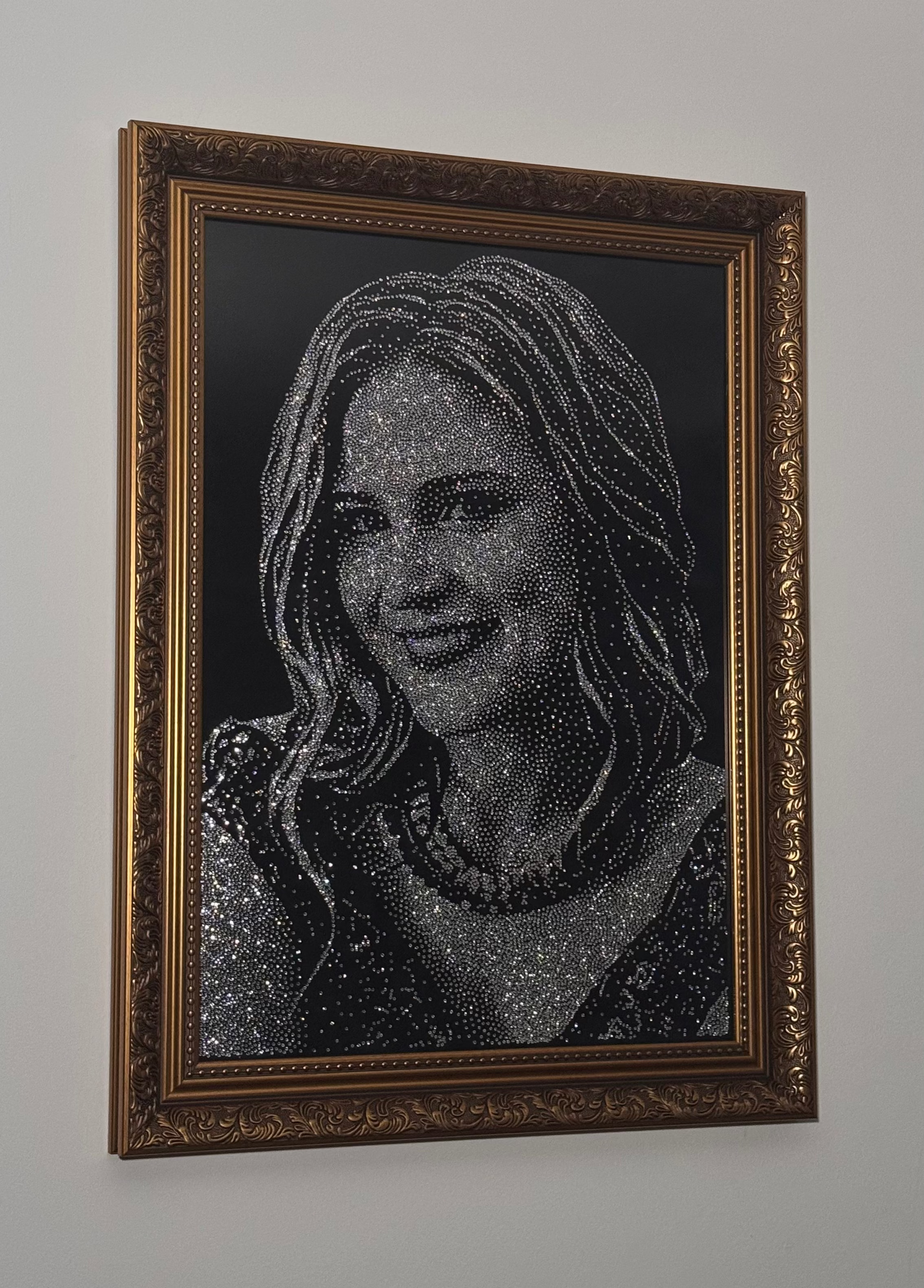 Framed portrait of a woman made from rhinestones on a plain wall