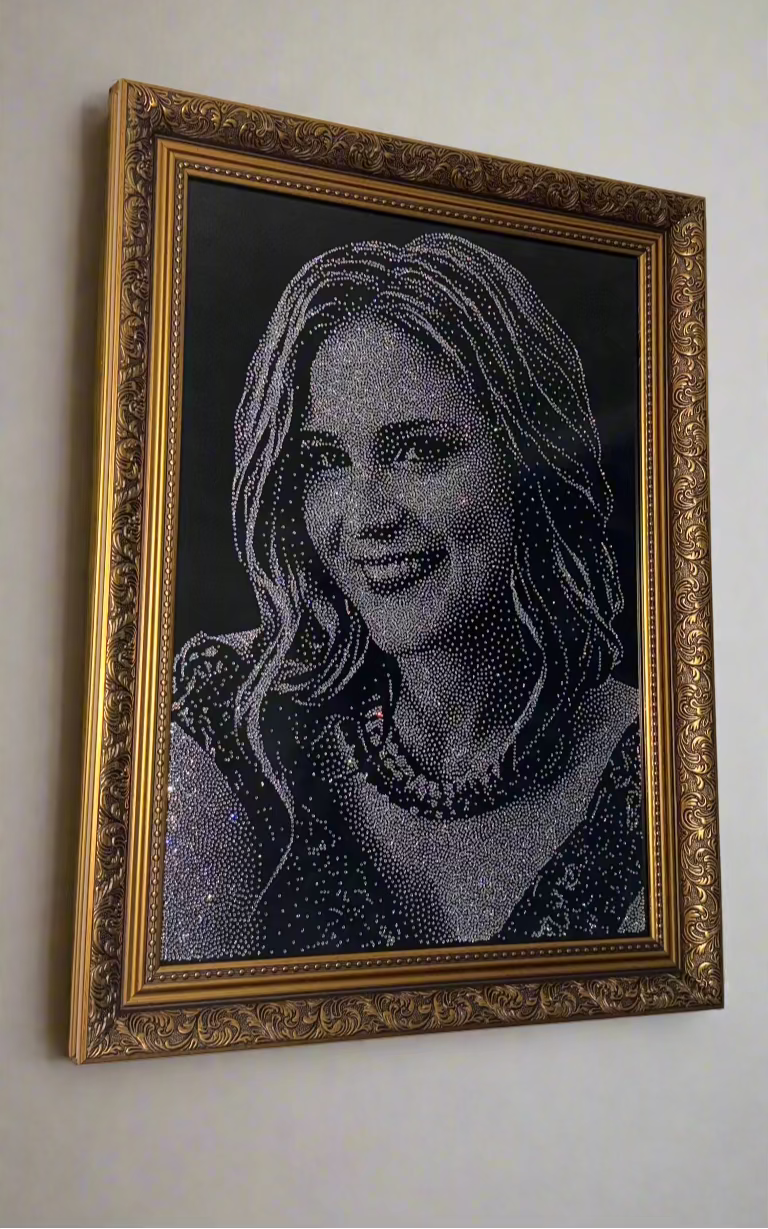 Framed portrait of a woman made from small beads or stones on a white wall.